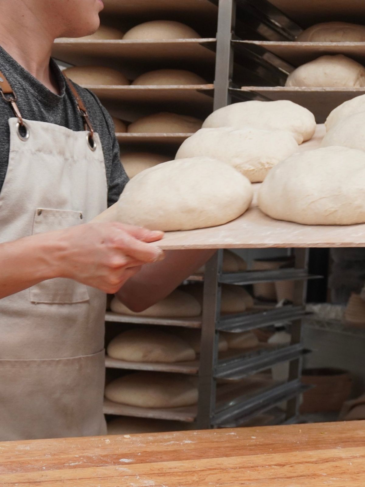 Panadero llevando hogazas de masa cruda en una pala de madera